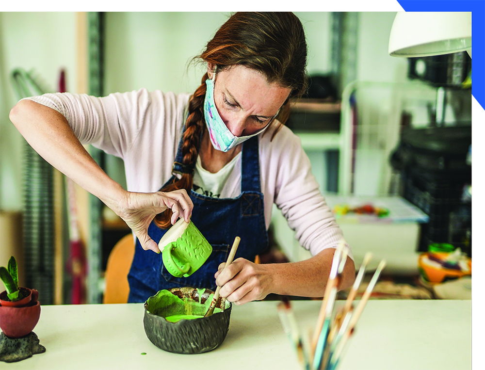 masked adult artist glazing a mug