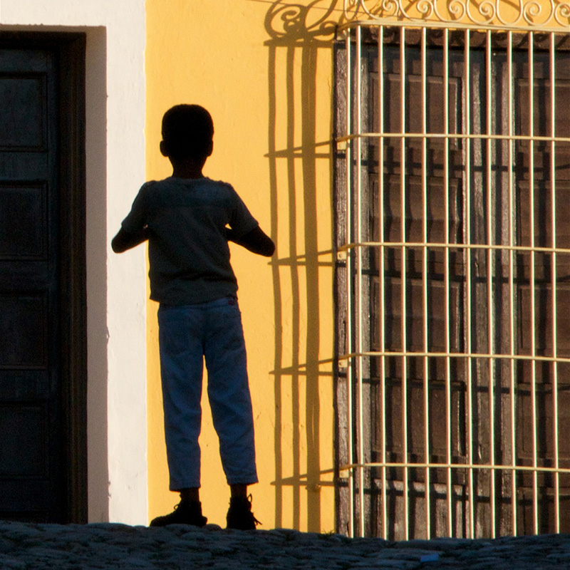 A young child standing in between a caged window and a door. Nancy Ori An Afternoon Memory, 2017 Archival inkjet photograph 18 x 18 inches