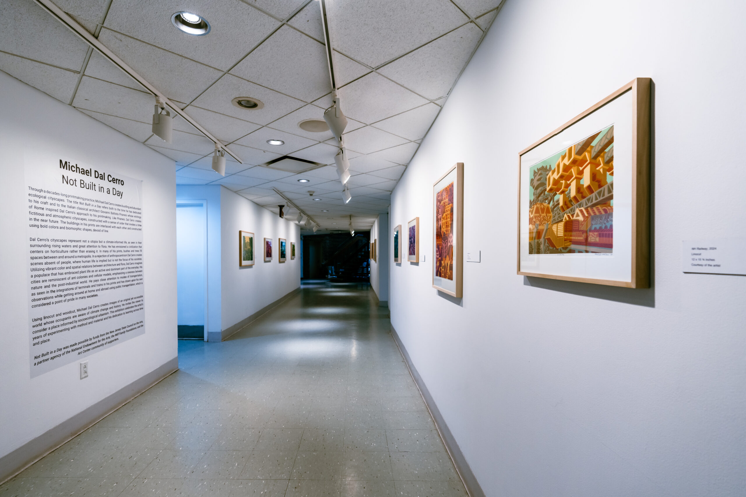 A long hallway with framed art work and a description of the process on the walls. The end of the hallway is pitch black.