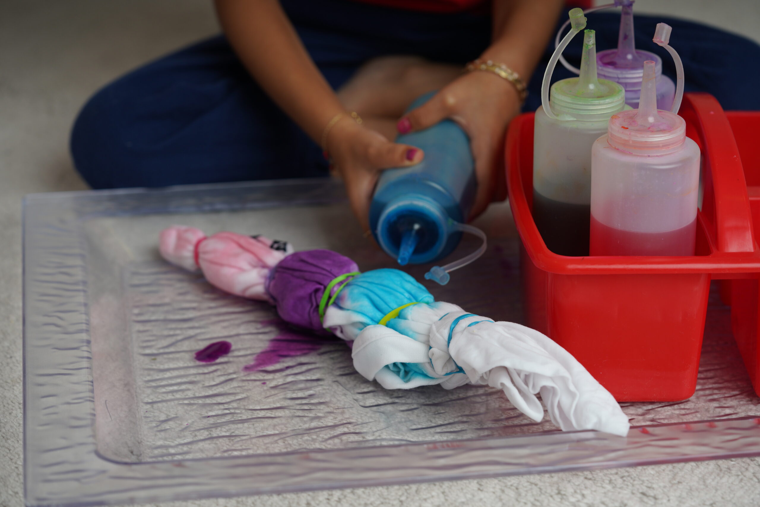 Little kid enjoying making a craft, using different colour ink to paint a tie-dyed cloth. Kids arts and crafts, Tie dye—art and craft DIY for children concept. Artist taking an online art class